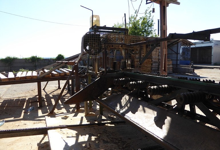 Горизонтальный ленточный станок отпиливает третью горбыльную доску, формируя трехстороннюю призму